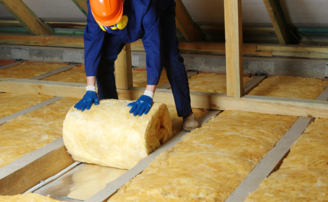 Construction worker thermally insulating house attic with glass wool